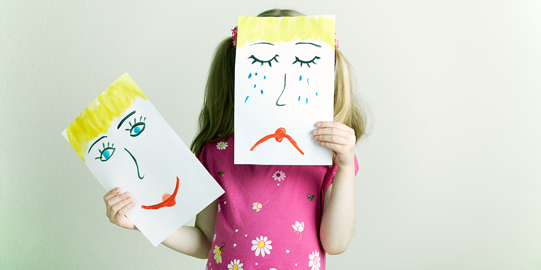 Ett förskolebarn håller upp två teckningar som illustrerar sorg och glädje