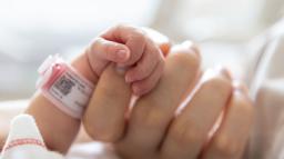 En för tidigt född baby griper om en vuxens hand.