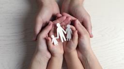 Händer håller skyddande i tre pappersfigurer av föräldrar med ett barn.