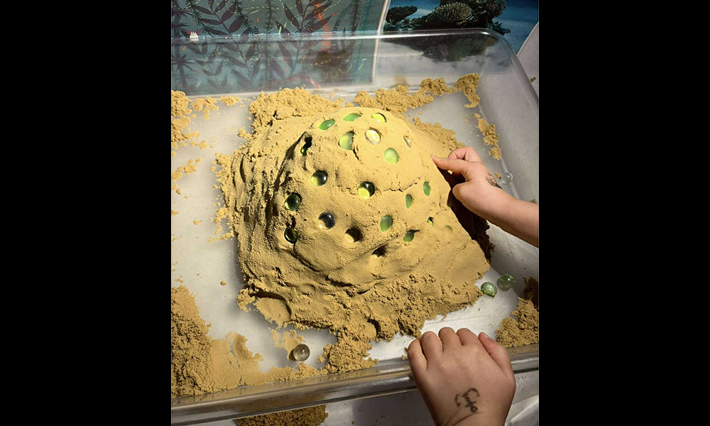 Ett barn som skapar i ateljen med sand och glaskulor.