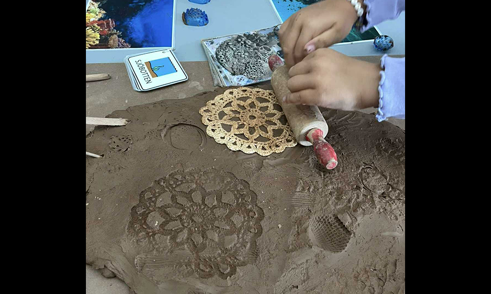 Barn som skapar i ateljén genom att kavla ut mönster i lera.