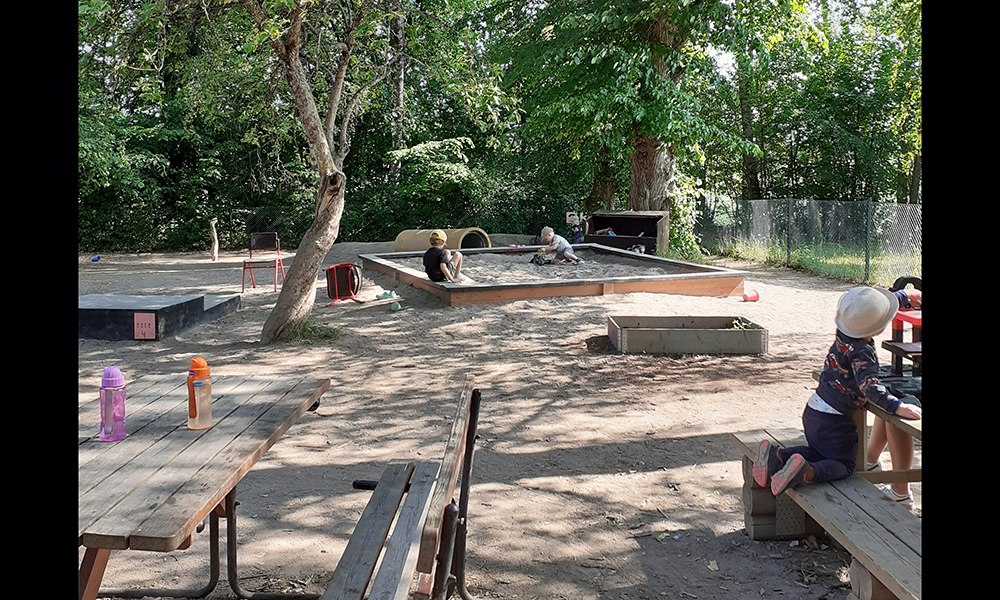 Sandlåda, bord och bänkar på förskolans lummiga gård.