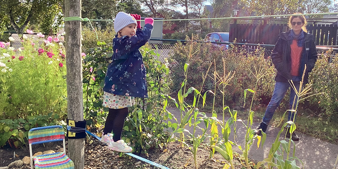 Flicka som balanserar på en lina i skogsträdgården.