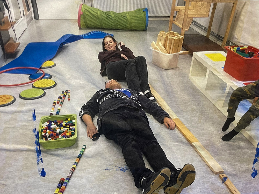 Förskollärare Tomas Bolting förskollärare och barnskötarpraktikanten Wilma Falck ligger på ett golv och visar hur stor en delfin är.