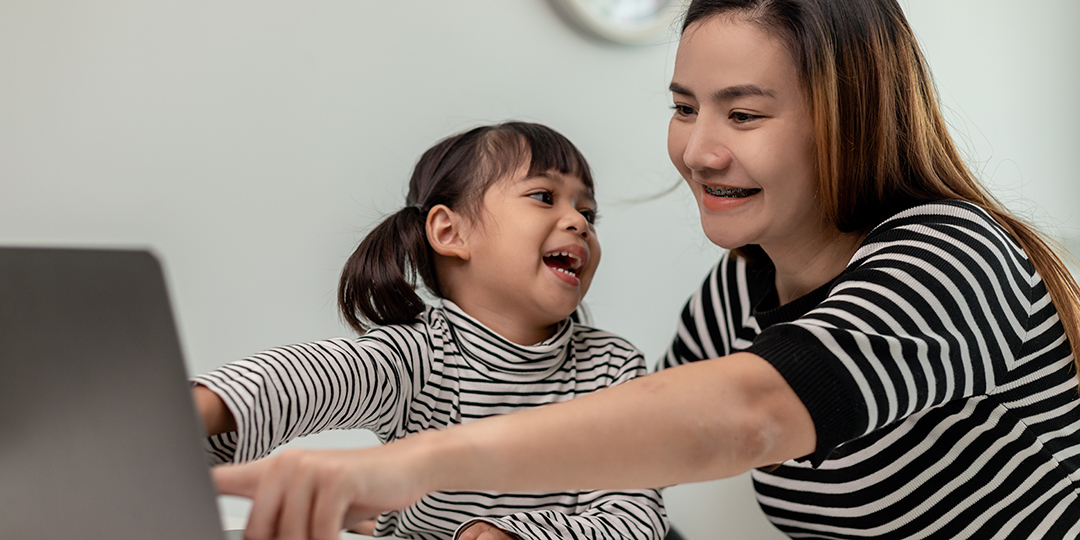En flicka med mamma sitter framför datorn och har ett lekmöte med förskolan.