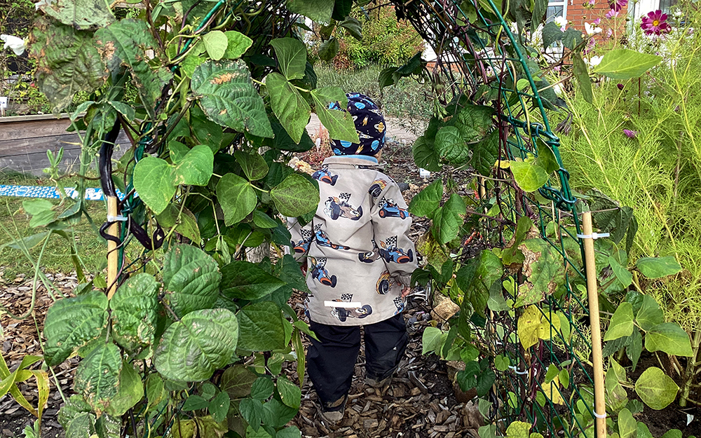 Ett litet barn går igenom en växtbåge full av gröna blad.