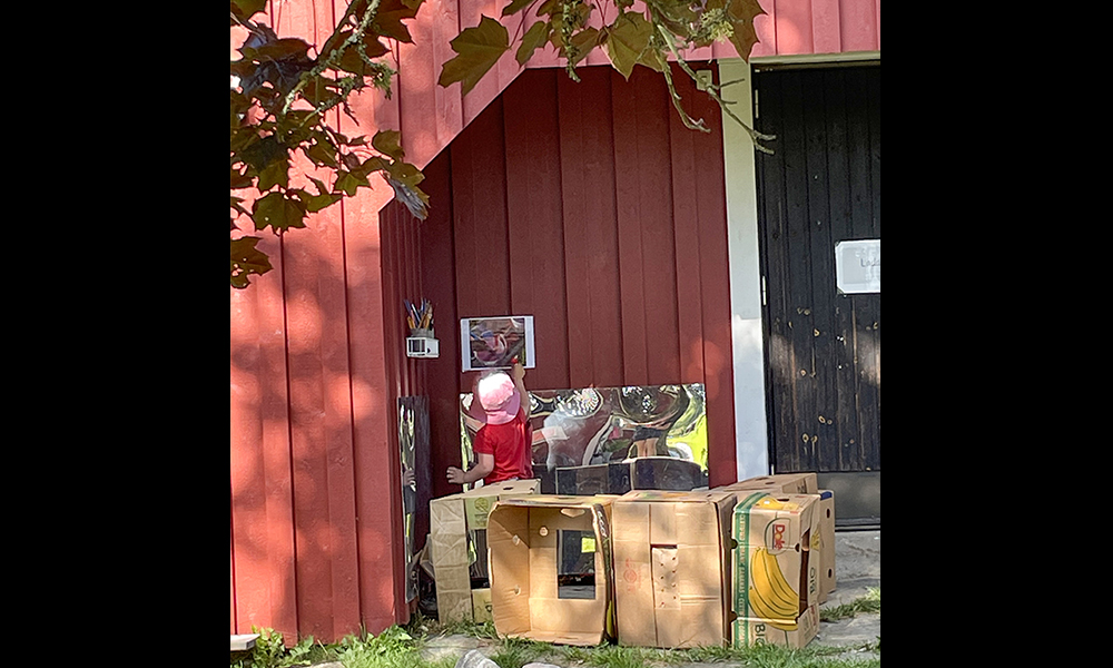 Bild som visar en utomhuskoja gjord av kartonger med ett barn som leker.