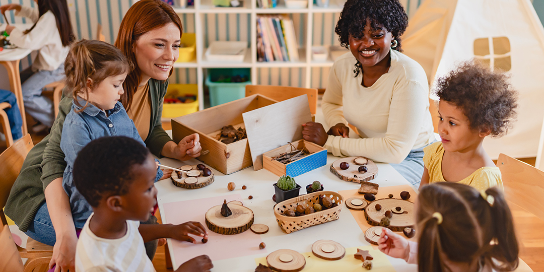 En grupp barn med två pedagoger som sitter och pysslar vid ett bord.