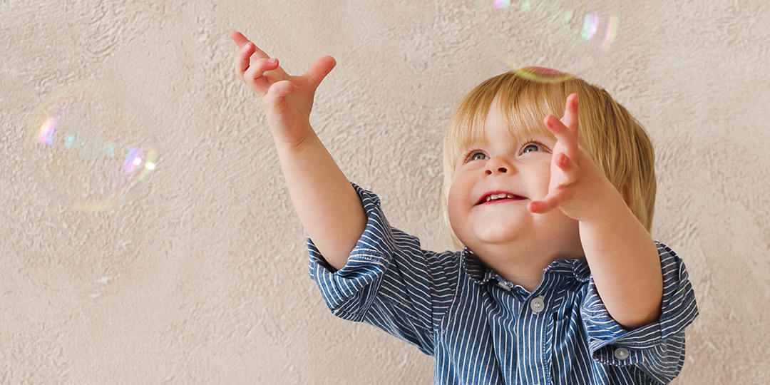 Bild som visar ett litet barn som försöker nå såpubblor inomhus.