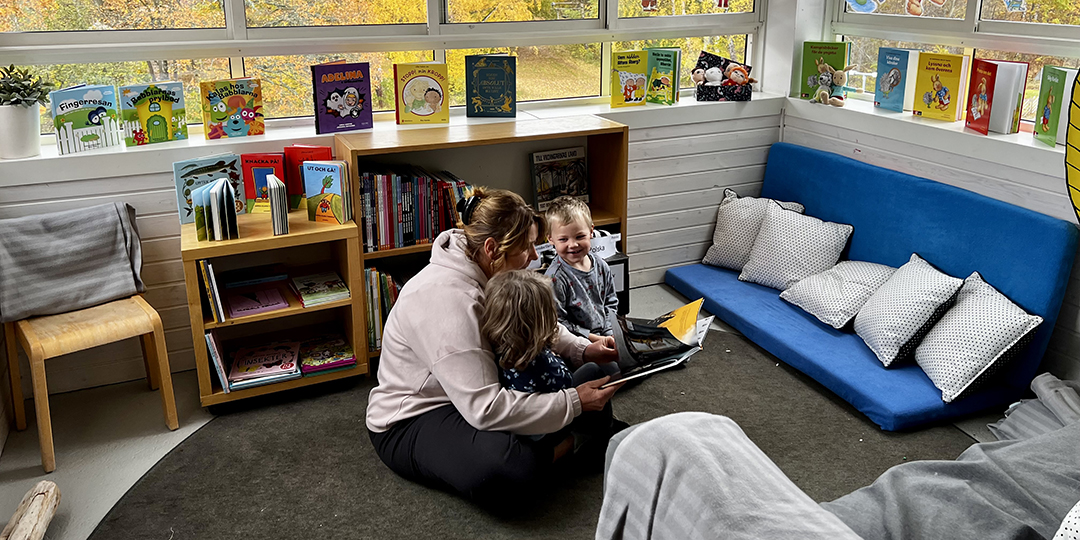Vuxen läser böcekr för två barn i förskolans läshörna.