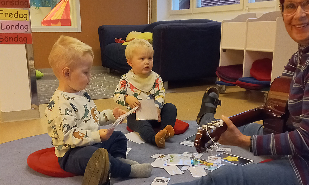 Två barn och pedagog som spelar gitarr.