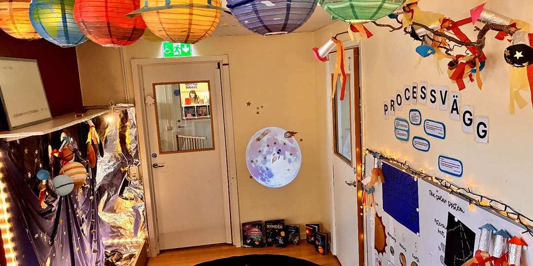 Rymdtema på Åmmebergs förskola där rislamporna i taket har blivit planeter. Till höger processväggen med barnens reflektioner.