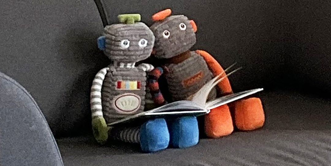 Mjuka robotdockor läser bok i soffa.