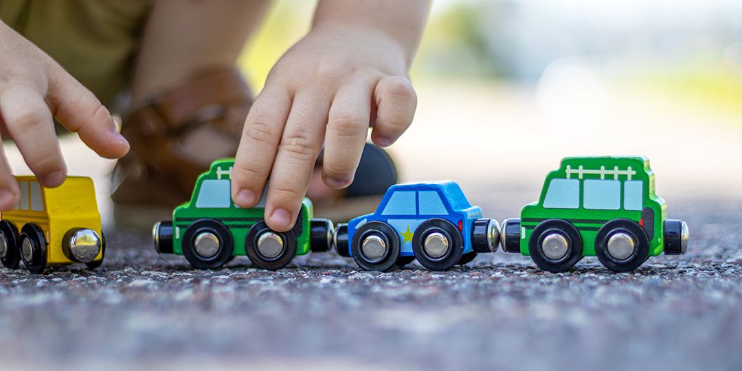 Ett barn sitter på huk utomhus och leker med leksaksbilar i trä.