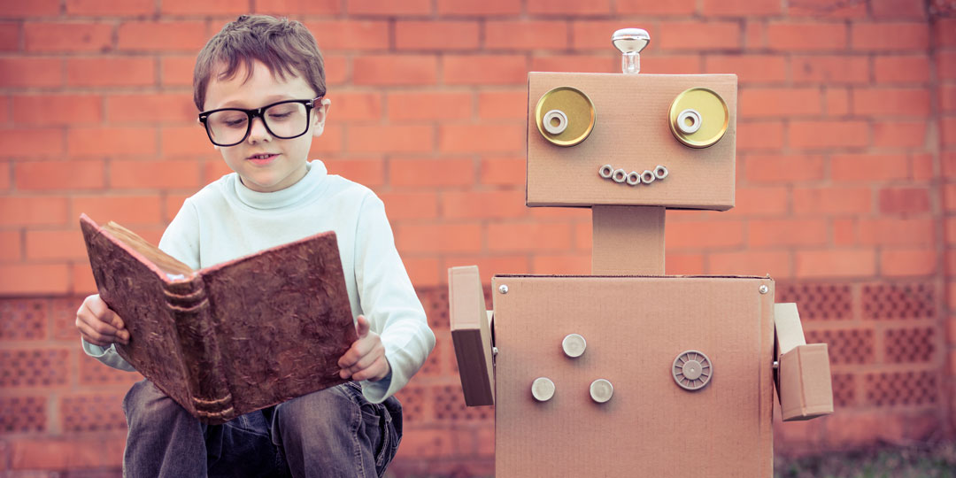 Pojke sitter och läser bredvid en robot gjord i kartong.