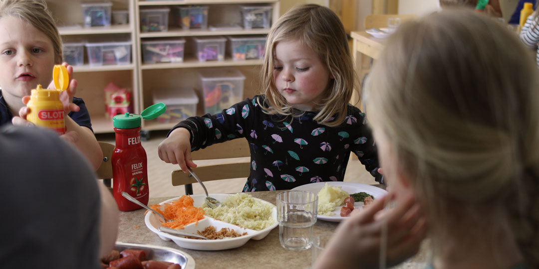 Lunch på förskolan. Ett barn tar grönsaker ur ett fat.