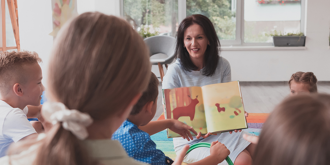 En pedagog visar ett uppslag i en barnbok för en liten grupp barn.