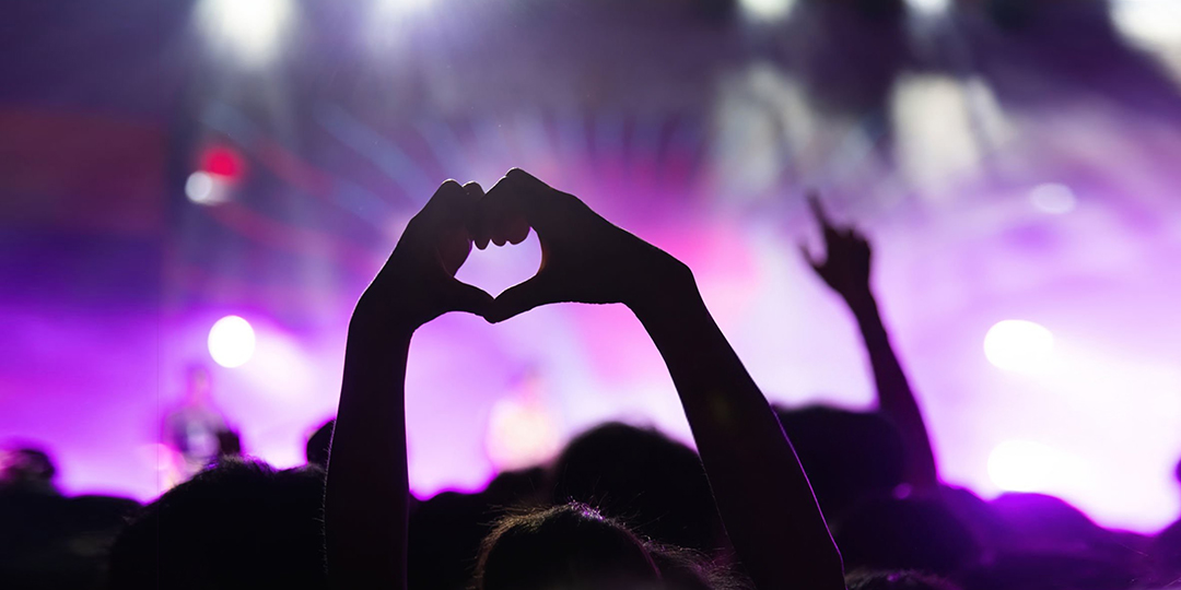 Två händer formar ett hjärta i ett publikhav på en musikfestival.