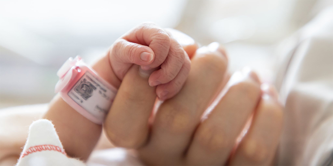 En för tidigt född baby griper om en vuxens hand.