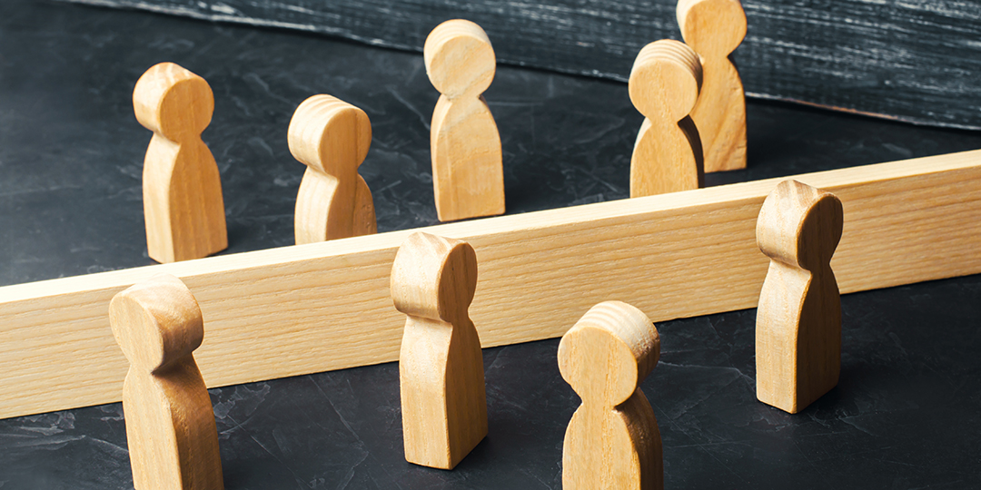 Två grupper träfigurer på var sin sida om ett staket.