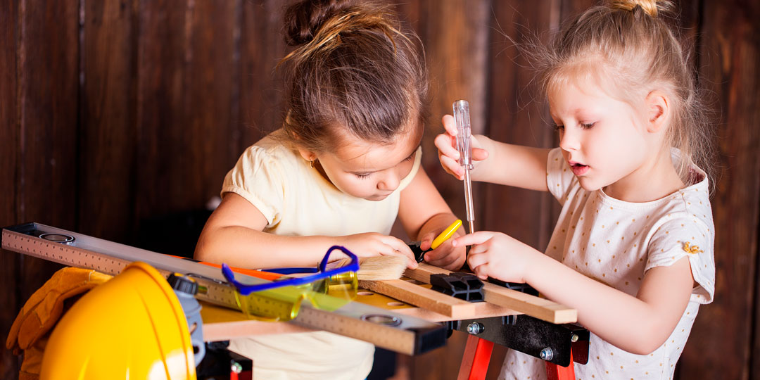 Två flickor i förskoleålder arbetar med verktyg vid en arbetsbänk anpassad för barn.