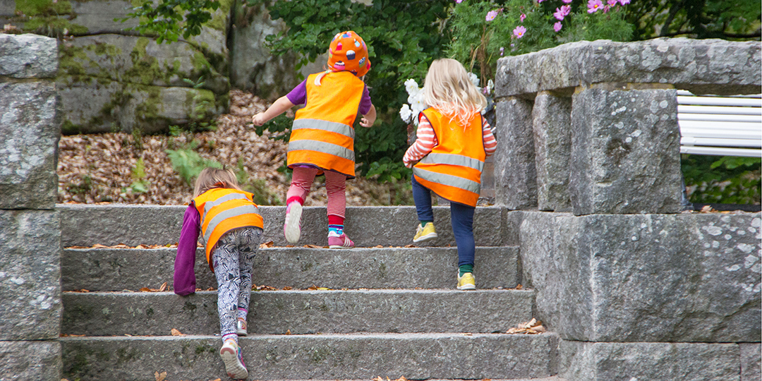 Tre förskolebarn springer uppför en stentrappa.