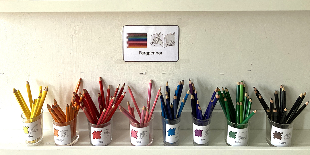 Målarpennor sorterade efter färg i burkar märkta med bildstödskort.