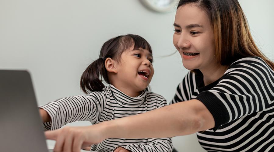 En flicka med mamma sitter framför datorn och har ett lekmöte med förskolan.