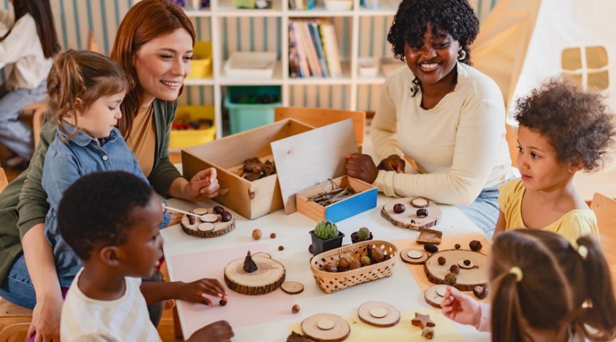 En grupp barn med två pedagoger som sitter och pysslar vid ett bord.