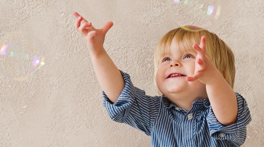 Bild som visar ett litet barn som försöker nå såpubblor inomhus.