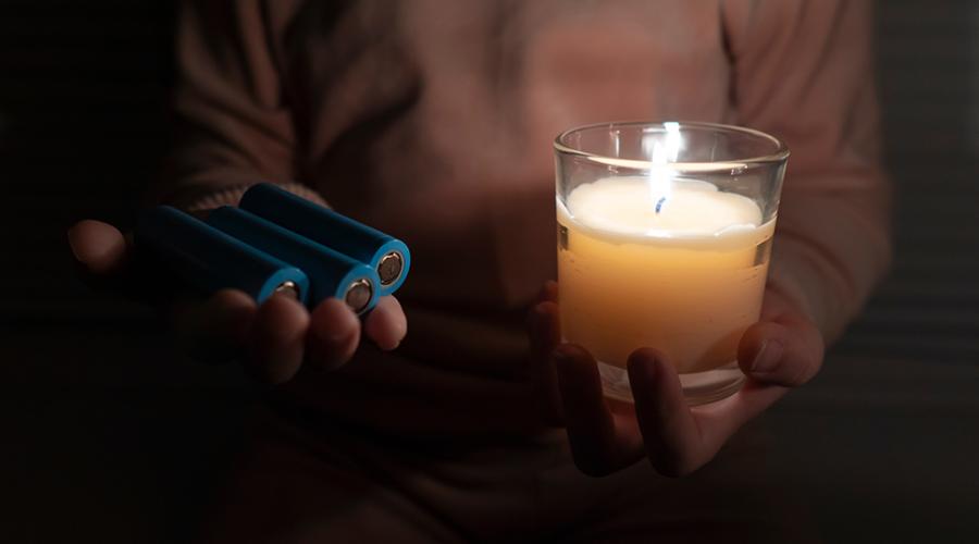 Ett barn i ett mörkt rum håller i ett stearinljus och batterier.