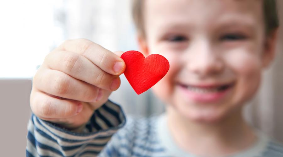 Glad förskolepojke håller upp ett rött pappershjärta.
