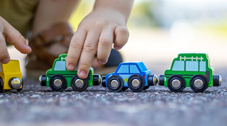 Ett barn sitter på huk utomhus och leker med leksaksbilar i trä.