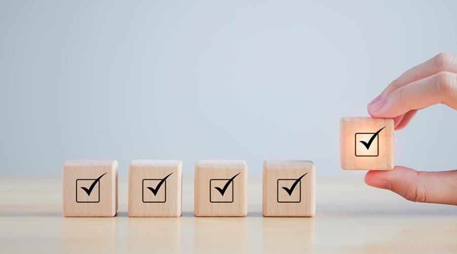 En hand placerar träklossar med checkboxsymboler på en bordsyta.
