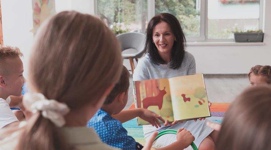 En pedagog visar ett uppslag i en barnbok för en liten grupp barn.