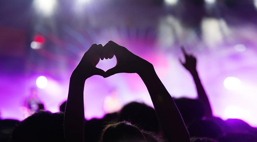 Två händer formar ett hjärta i ett publikhav på en musikfestival.
