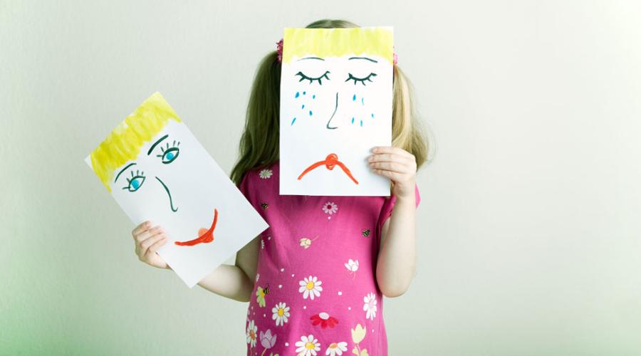 Flicka som håller teckning på ledset ansikte framför sitt ansikte, och en teckning med glatt ansikte i andra handen.