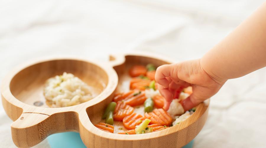 Barnhand griper efter en grönsaksbit från en tallrik.