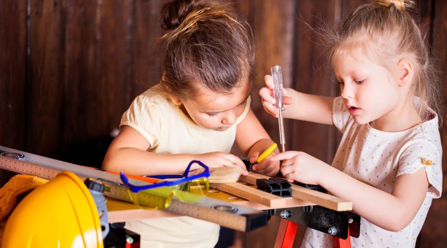Två flickor i förskoleålder arbetar med verktyg vid en arbetsbänk anpassad för barn.