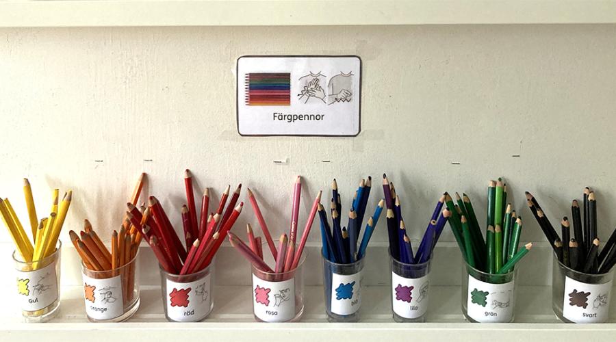 Målarpennor sorterade efter färg i burkar märkta med bildstödskort.