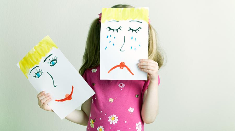 Ett förskolebarn håller upp två teckningar som illustrerar sorg och glädje