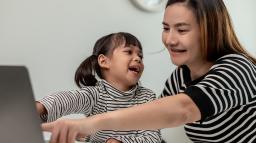 En flicka med mamma sitter framför datorn och har ett lekmöte med förskolan.