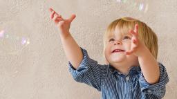 Bild som visar ett litet barn som försöker nå såpubblor inomhus.