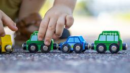 Ett barn sitter på huk utomhus och leker med leksaksbilar i trä.