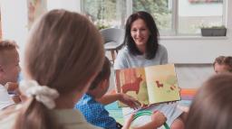 En pedagog visar ett uppslag i en barnbok för en liten grupp barn.