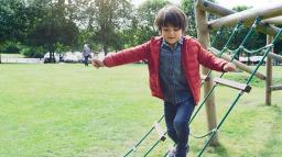 Pojke går balansgång på klätterställning i parken.