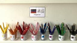 Målarpennor sorterade efter färg i burkar märkta med bildstödskort.