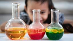Ett barn studerar färgade vätskor i tre glasbehållare.