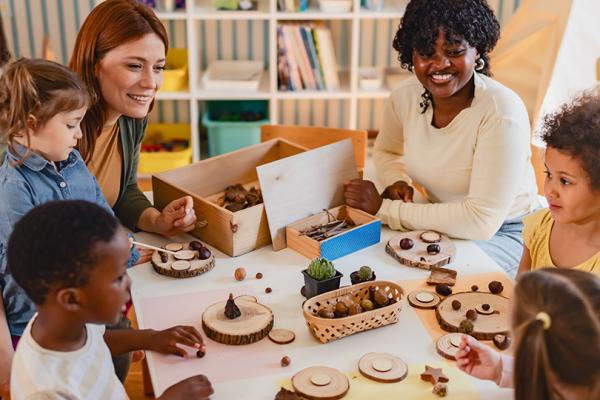 En grupp barn med två pedagoger som sitter och pysslar vid ett bord.