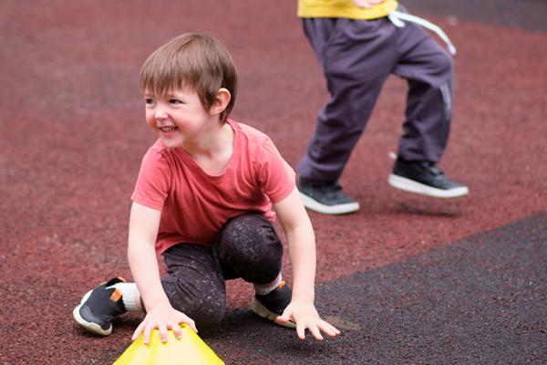 Två förskolebarn med gymnastikskor sitter och springer på löparbana.